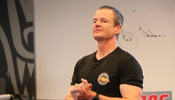 A man clapping with a slight smile in a black t-shirt.