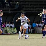 Women playing soccer at night on a field under lights.