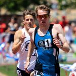Two athletes running in a race outdoors under sunny conditions.